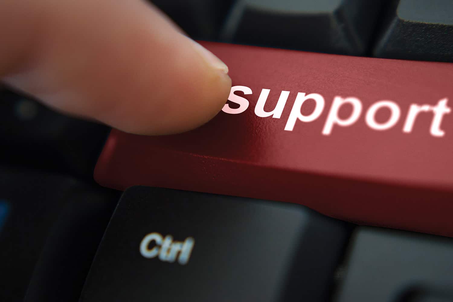 Finger resting on red ‘support’ button on a computer keyboard.