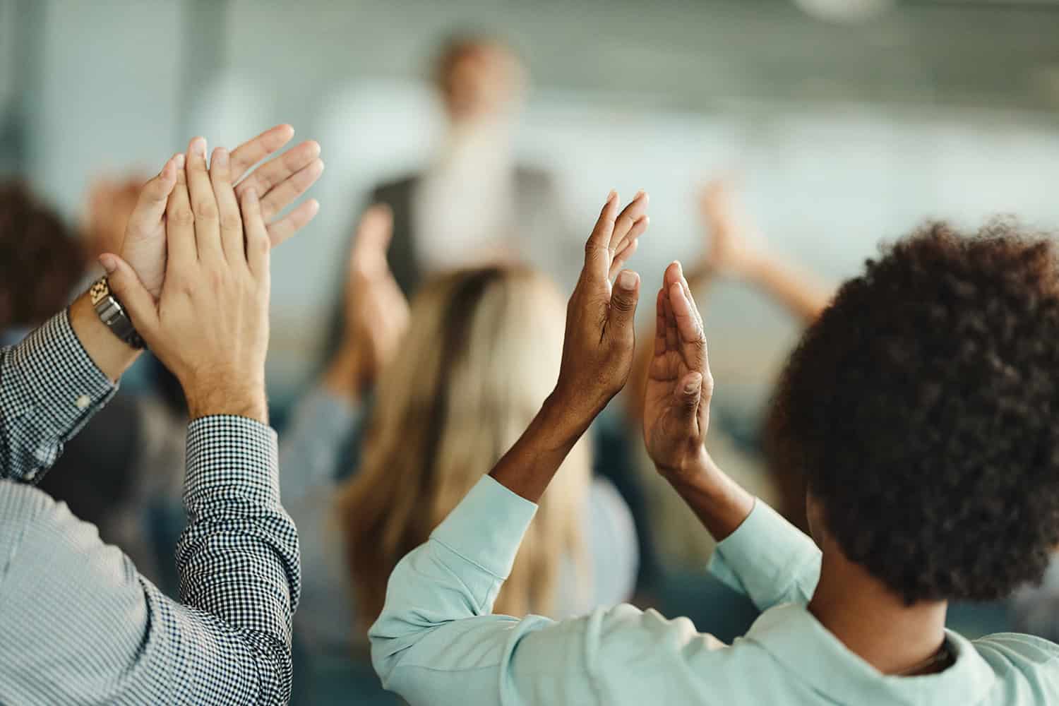 photo from behind of audience raising hands to clap a speaker, blurred in background