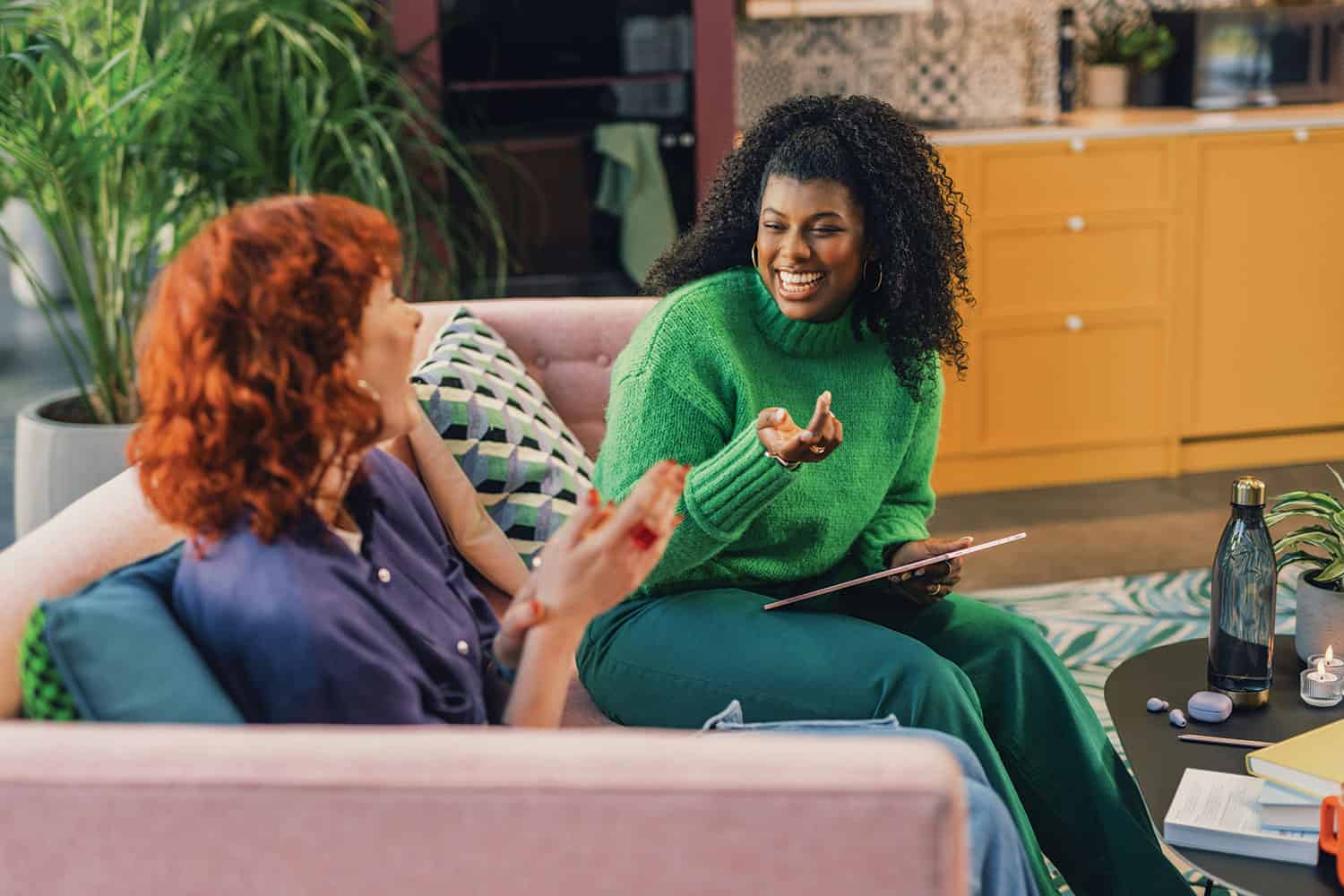 photo of two young women sitting on sofa chatting over a tablet about work