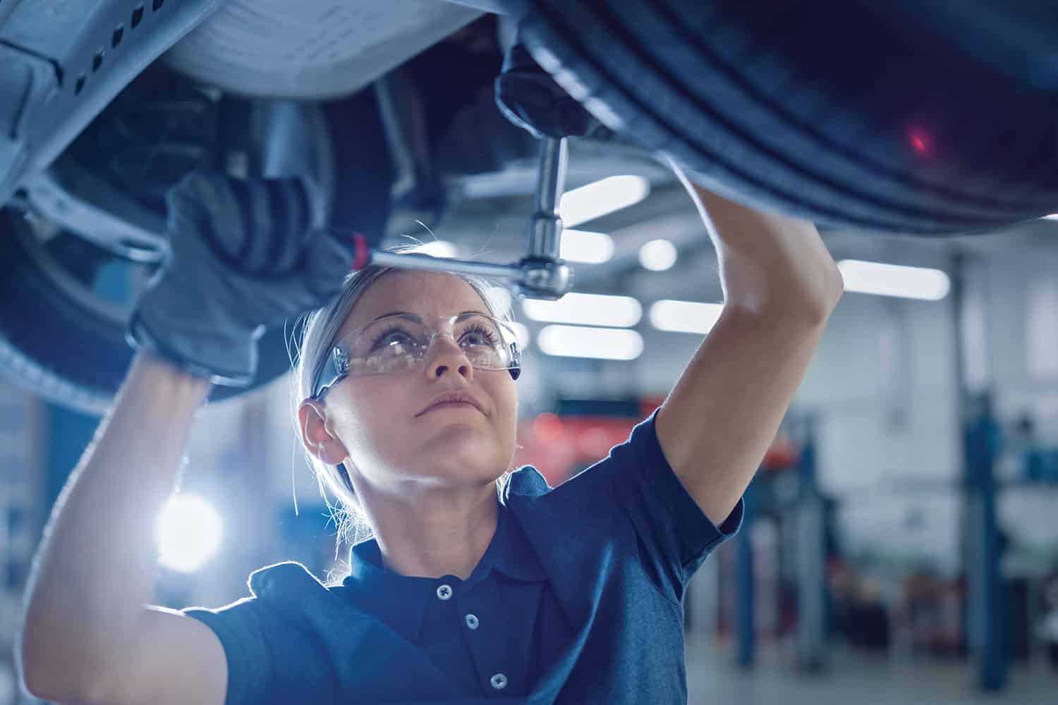 photo of female apprentice working on the underneath of a car jacked up in a garage