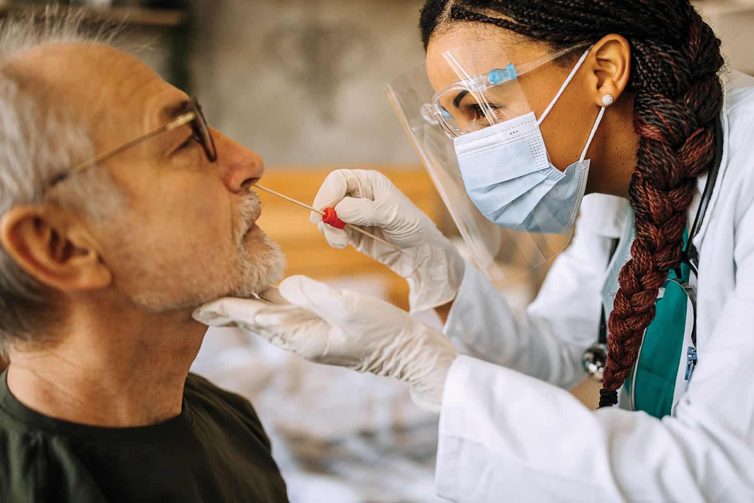 Photo of woman in face mask and gloves swabbing nose of older man