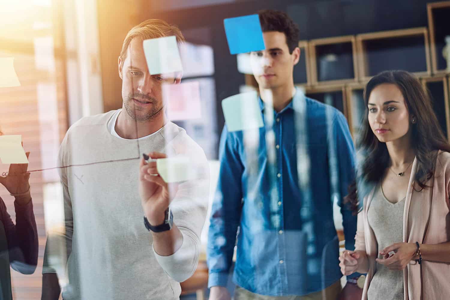 work colleagues planning together using post-it notes and drawing on a glass window