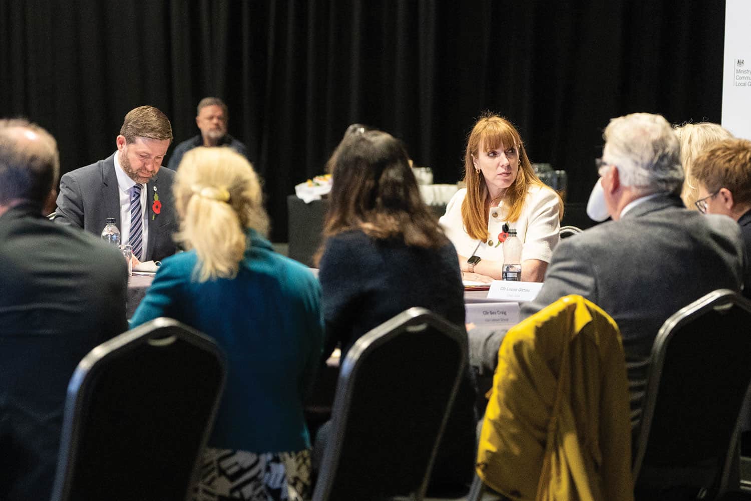 Behind LGA local government leaders seated at a meeting room table facing Deputy Prime Minister Angela Rayner and Local Government Minister Jim McMahon. COPYRIGHT MHCLG