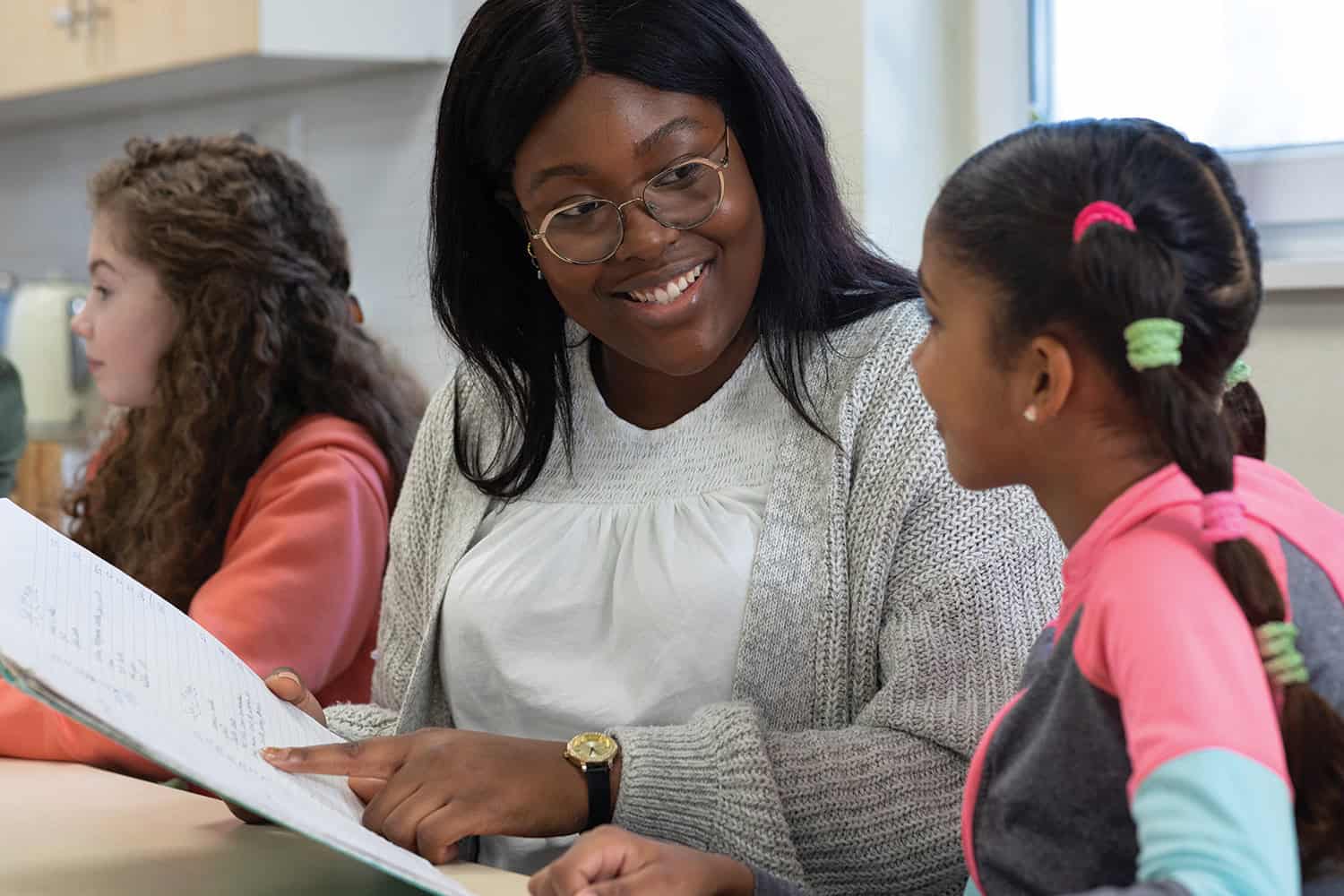 Woman social worker pointing to a book and smiling at young girl.