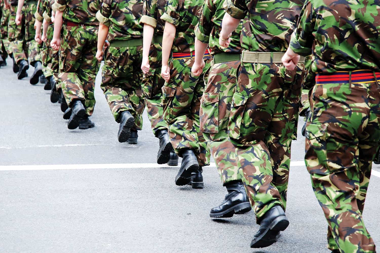 : detail of soldiers in camouflage and combat boots marching together, taken from shoulders down