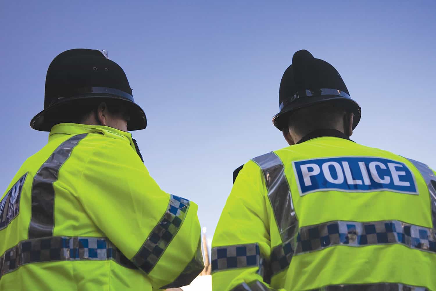 photo from behind of two police officers in helmets and high vis yellow jackets