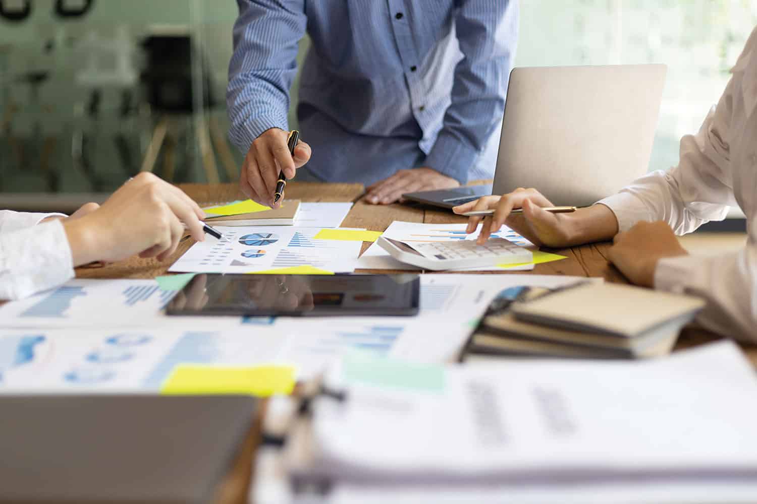 photo of team of people working together on plans and finance graphs and stats around an office table