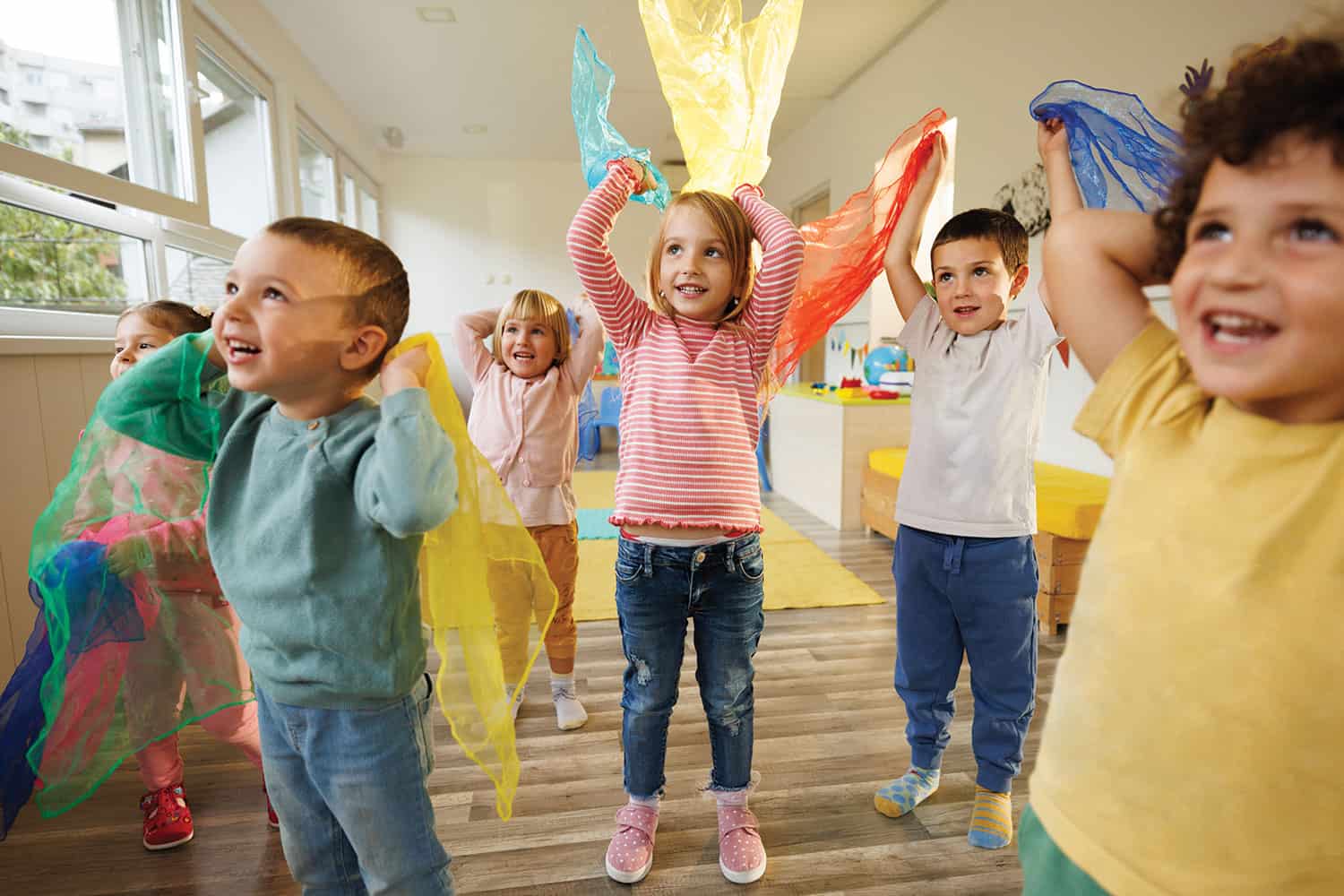 mix of young children playing with coloured scarves in school hall