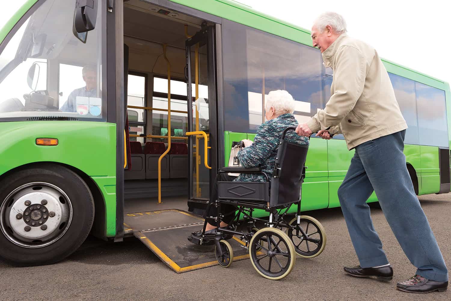photo of older man pushing older woman in wheelchair up ramp onto a green bus