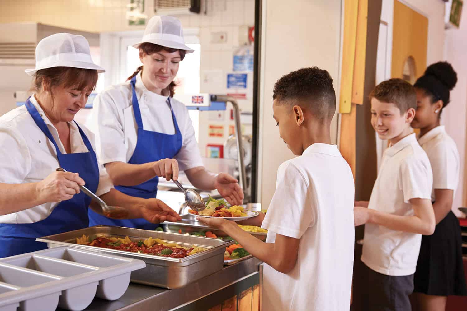 photo of mixed group of primary school children being served school dinners from a canteen servery point
