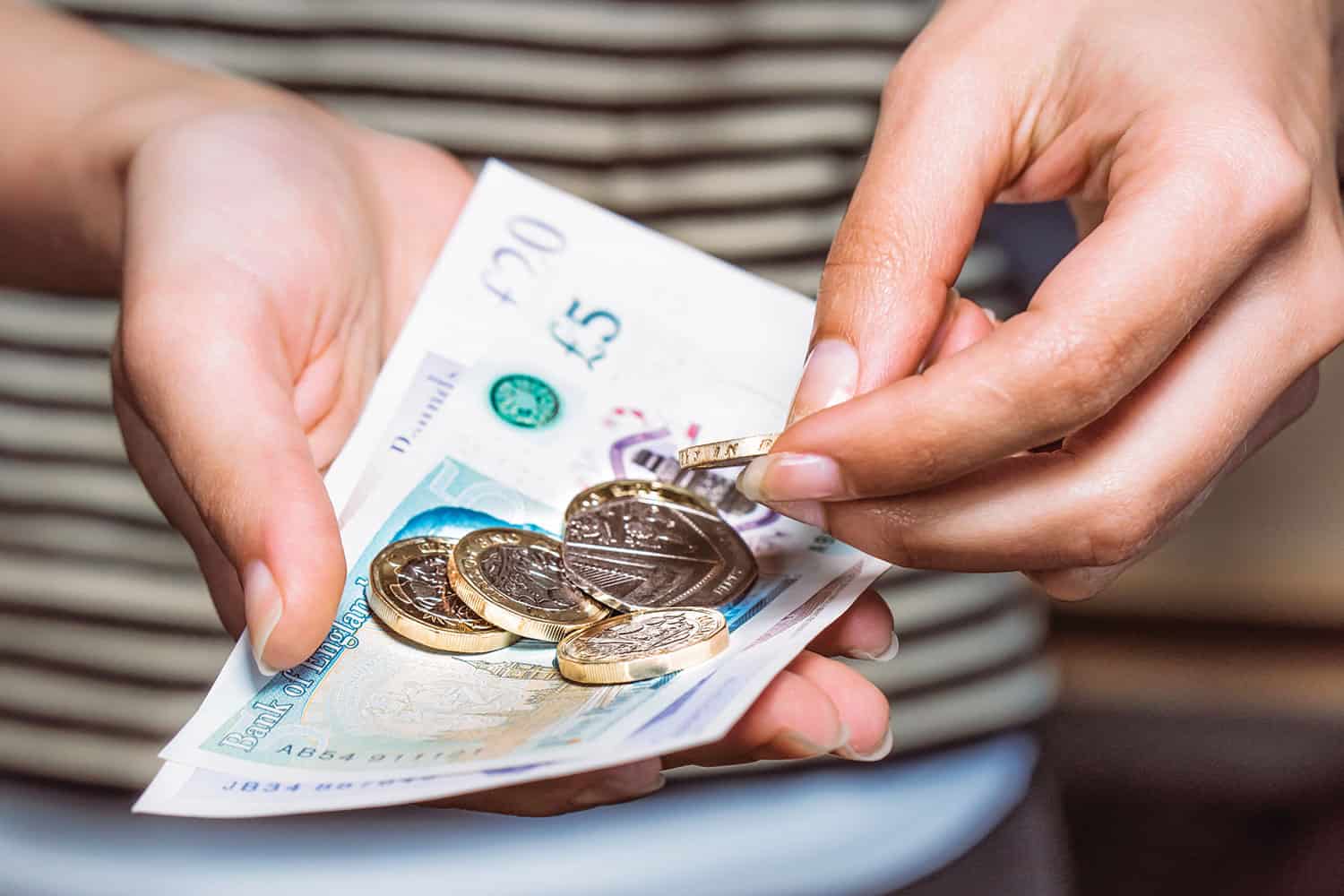 photo of hands holding five pound notes and one pound coins