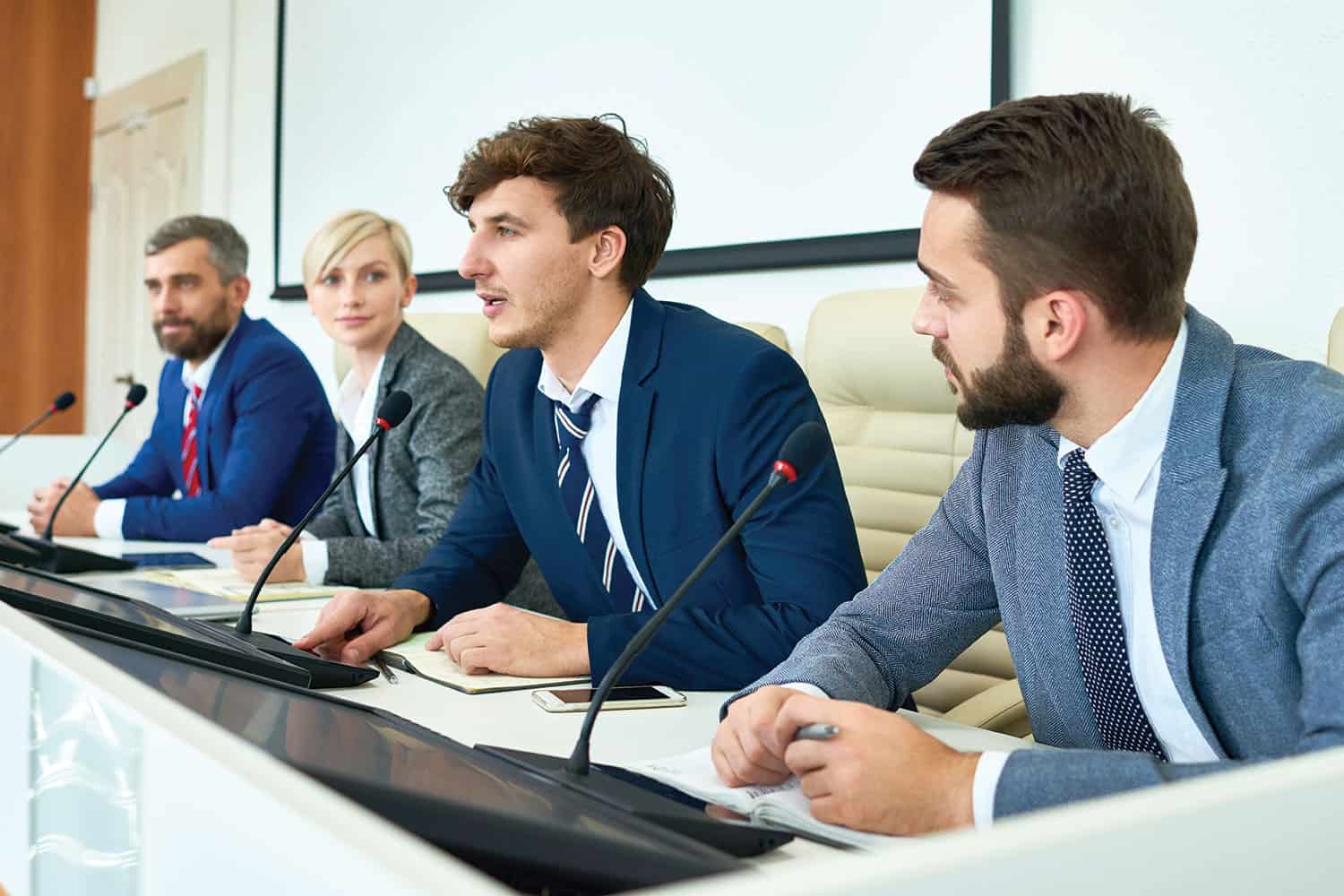 young male councillor making a point in a debate in a council chamber, speaking into a desk mic
