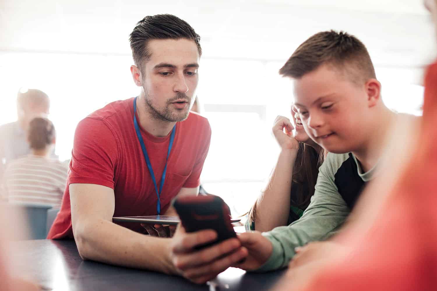 photo of young male teacher working with primary school-aged boy with special educational needs at classroom table