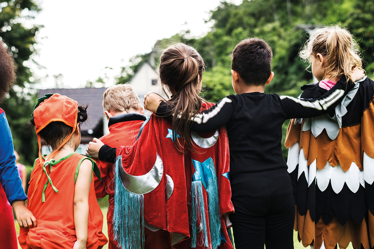 row of children viewed from behind, dressed up for Halloween, with their arms around each other