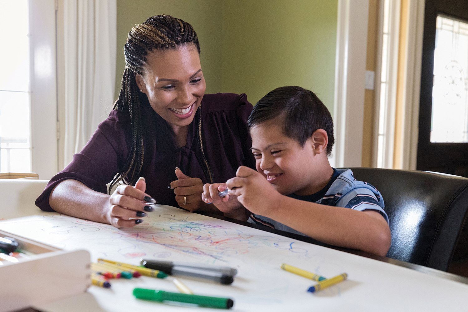 female social worker laughing and colouring at a table with a young boy with learning disabilities