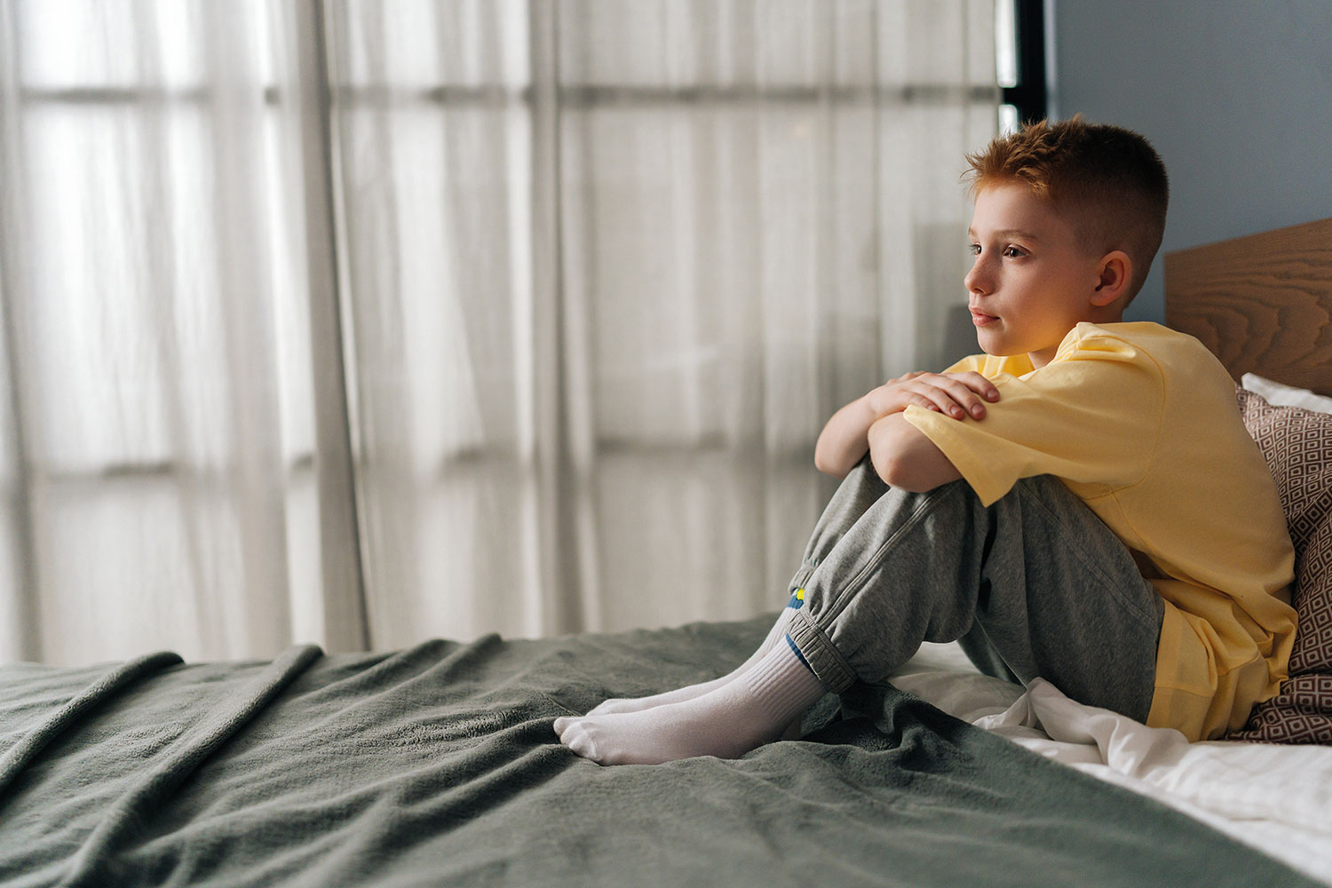 sad young boy sitting on bed in hotel room