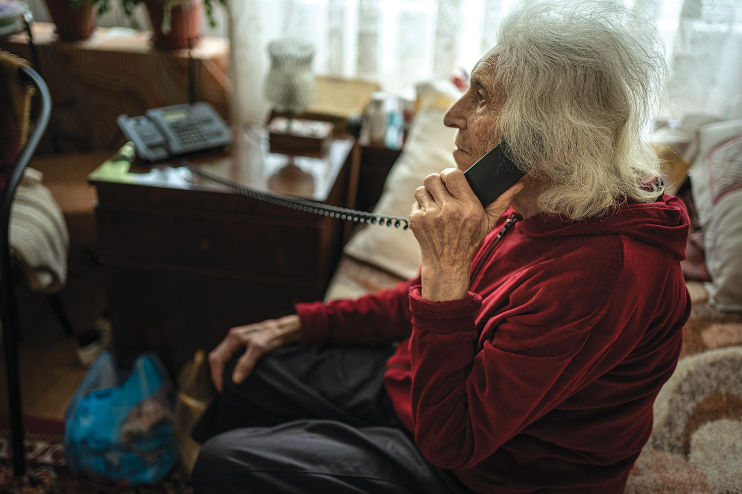 very old woman at home, sitting on her sofa on a landline telephone