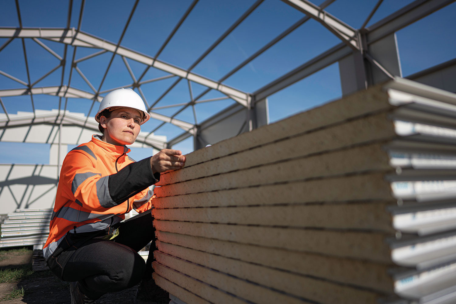 photo of woman construction worker in high-visibility jacket and safety helmet looking at stack of cladding panels