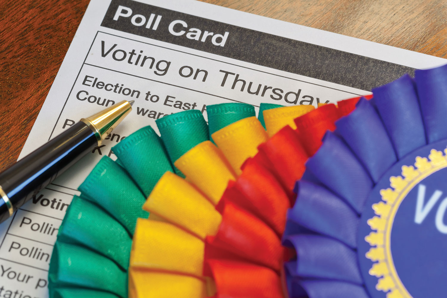 photo of a close-up of a ballot card, pen and coloured rosettes on a table