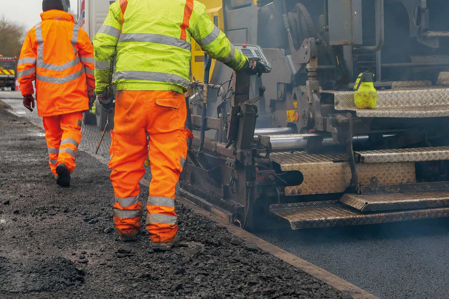 photo of workmen in high-vis coats and trousers working alongside road-surfacing machinery