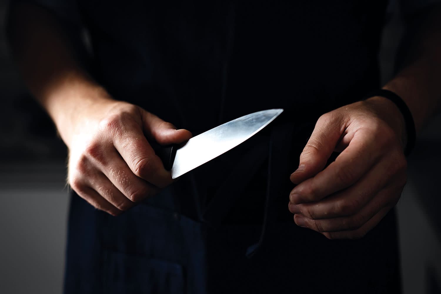 photo of close-up of hands emerging from darkness holding a knife